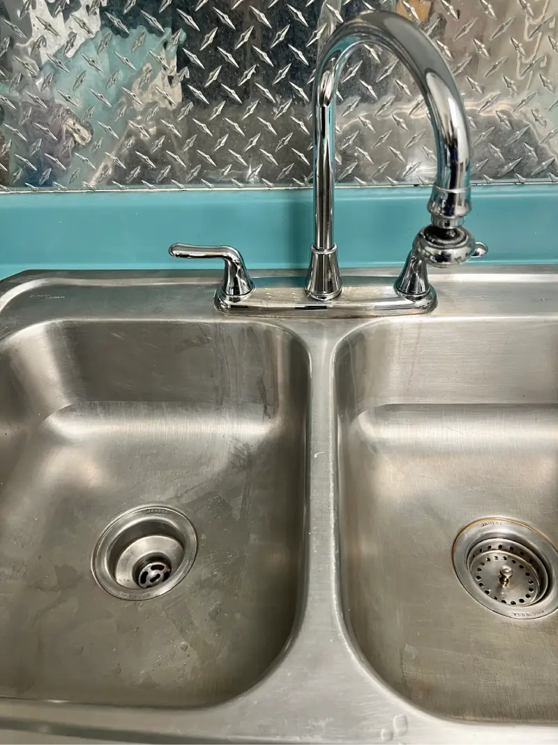 A double stainless steel kitchen sink with two faucets.
